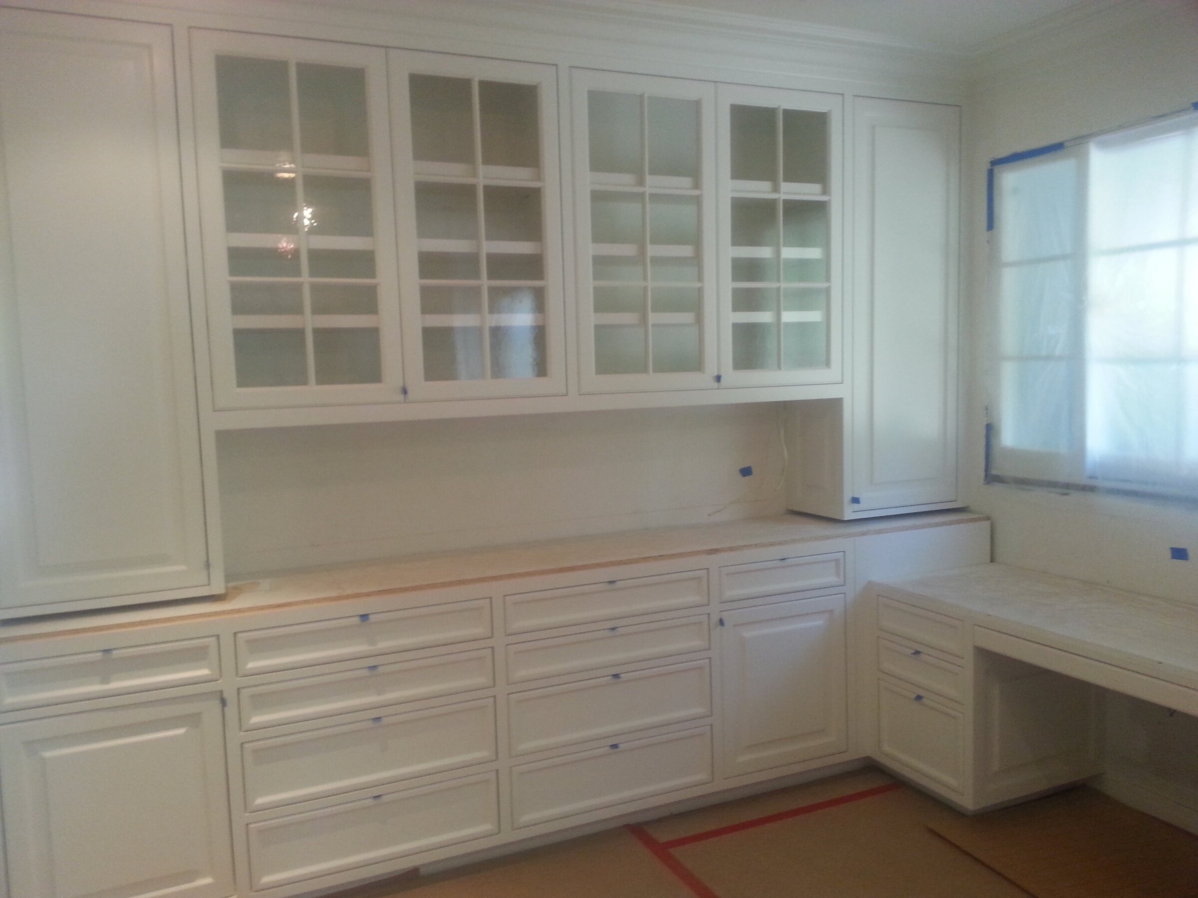 Large primed built-in hutch with mullioned glass-front upper cabinets, a full bank of drawers, and a knee-hole desk return