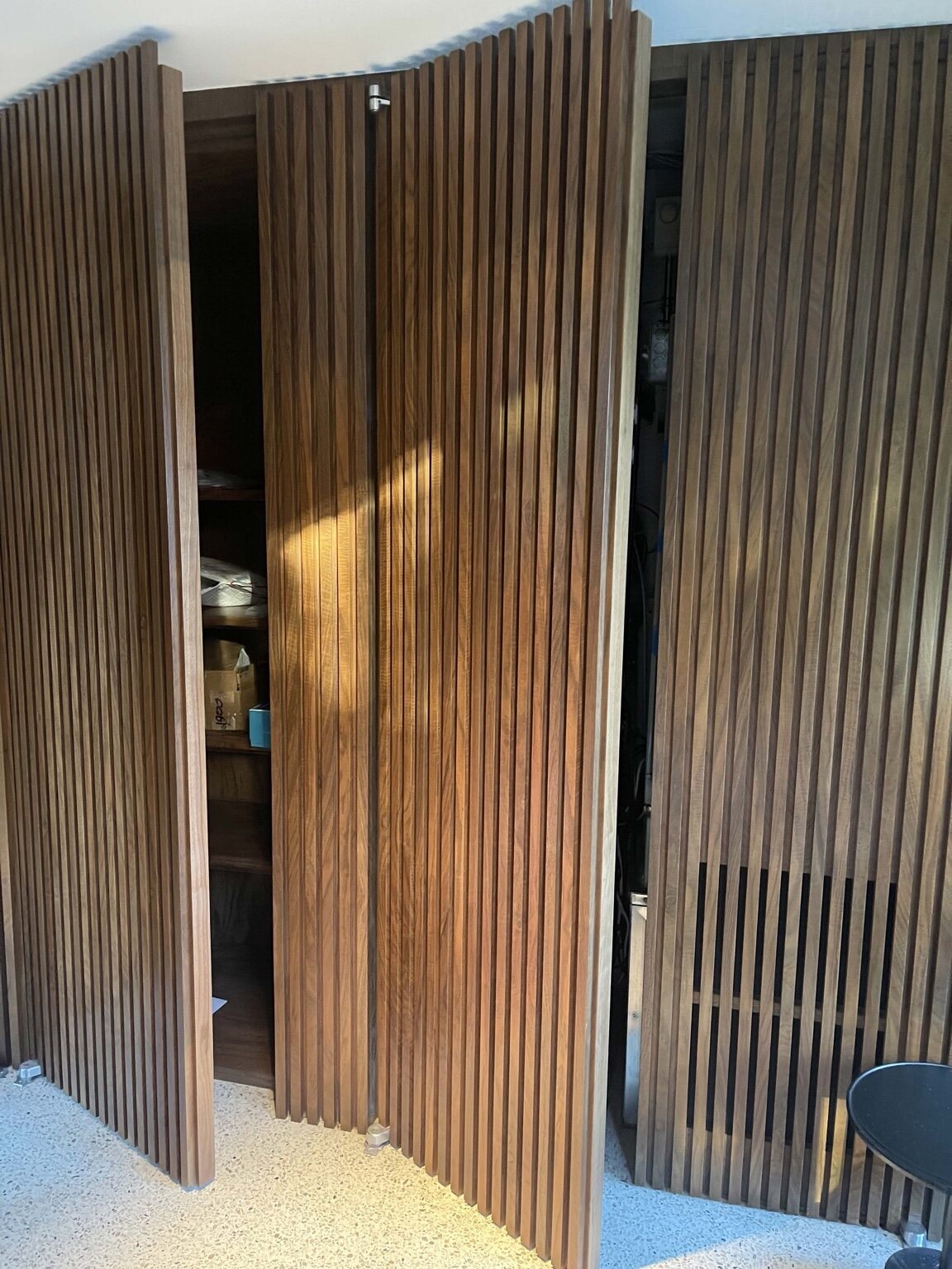 Floor-to-ceiling walnut slatted bi-fold doors concealing a custom storage system