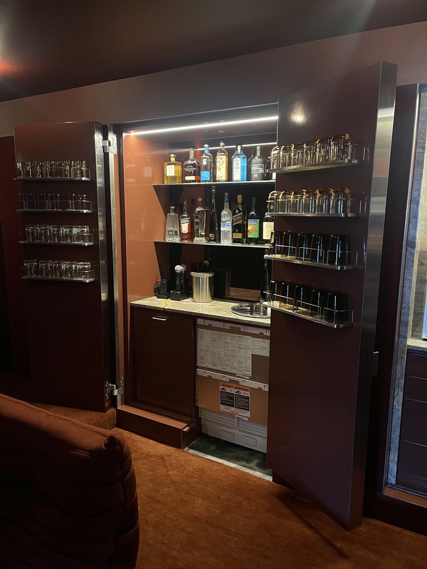 Deep merlot lacquered cabinet doors opening to a backlit built-in bar with glass racks, liquor shelves, and stone counter