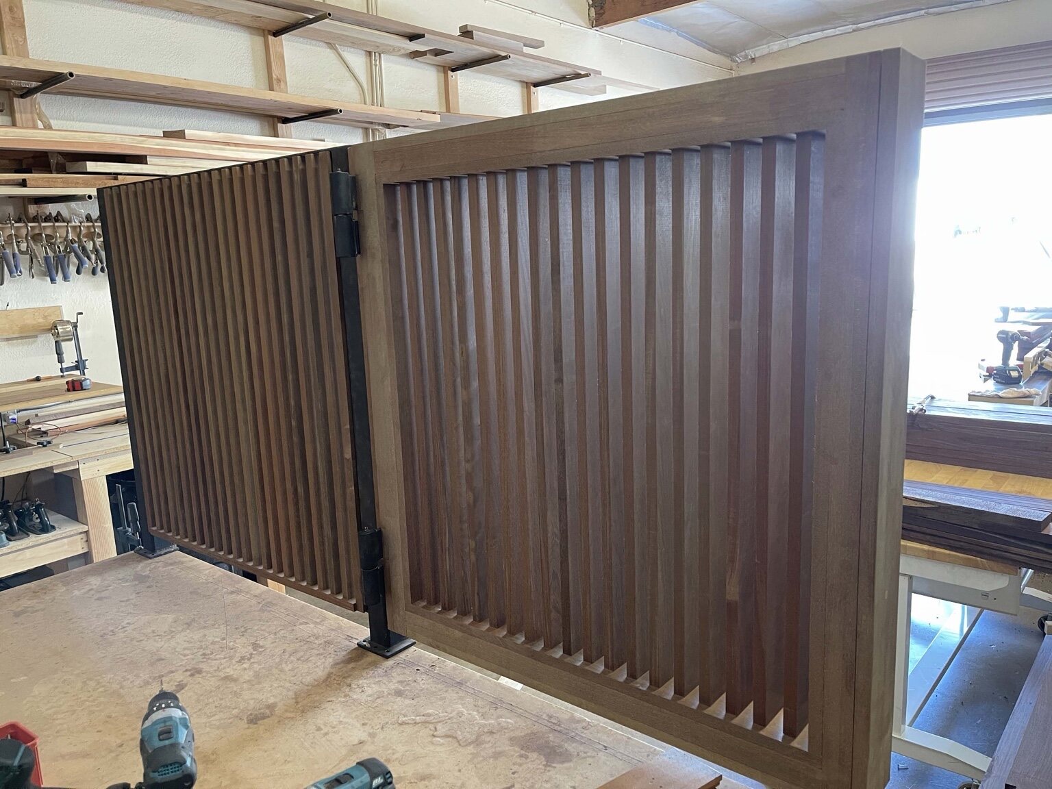 Framed custom wood bi-fold panels with vertical slats and a black steel pivot hinge, shown in the workshop