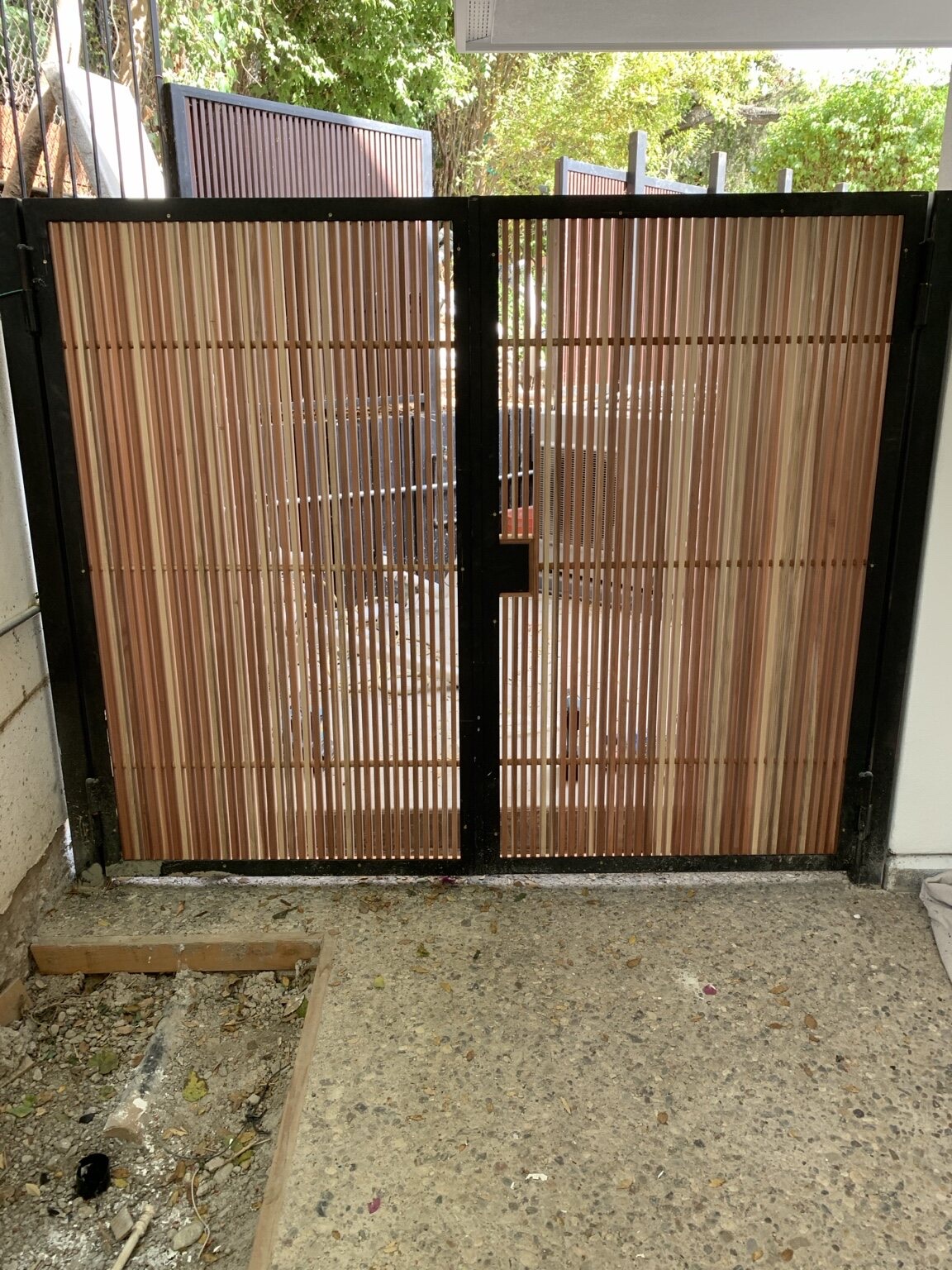 Double entry gates with vertical wood slats set in black steel frames, installed at an exterior walkway