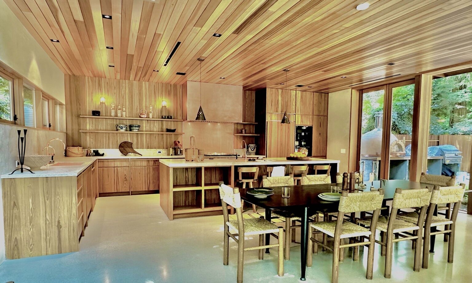 Custom wood kitchen with a slatted wood ceiling, natural wood cabinetry, and a large island opening to greenery
