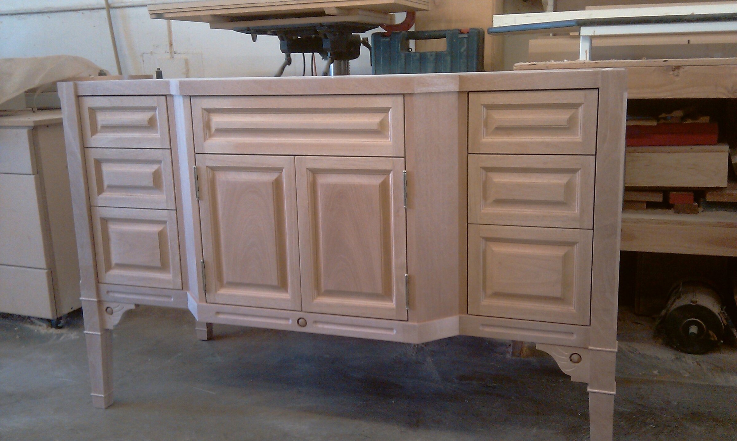 Unfinished solid-wood vanity in the workshop with raised-panel doors, banks of drawers, decorative molding, and tapered legs