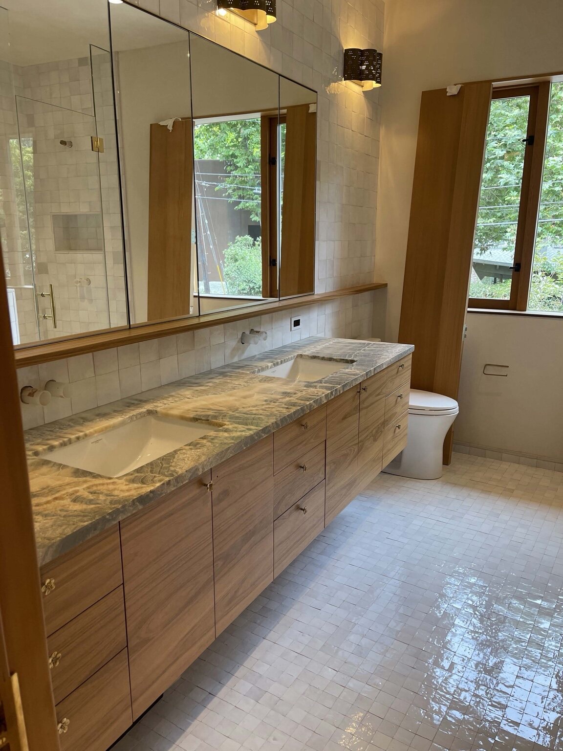 Floating custom wood double vanity with a dramatic blue-grey marble countertop, two undermount sinks, and a wall-mounted mirrored cabinet in a marble-tiled bathroom