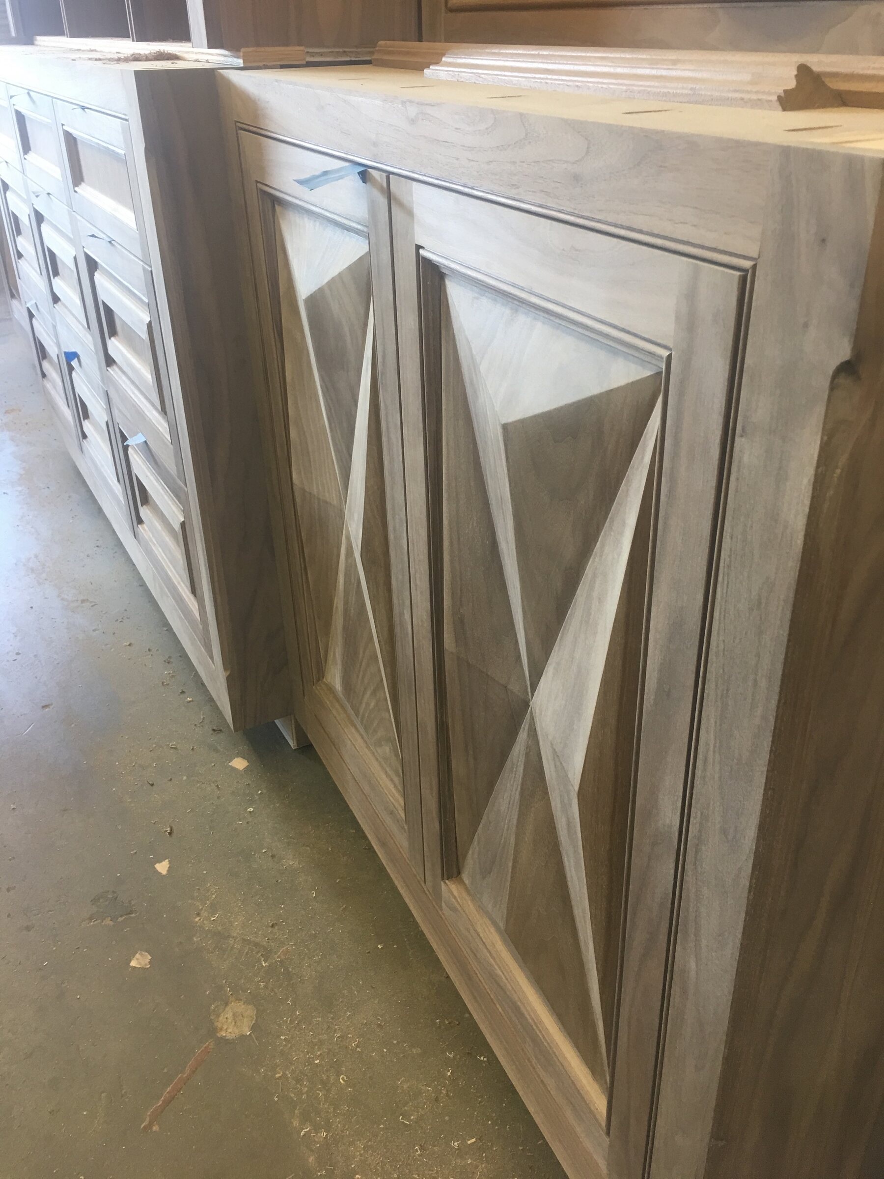 Close-up of a custom wood sideboard with striking diamond bookmatched veneer door panels alongside a bank of drawers in the workshop